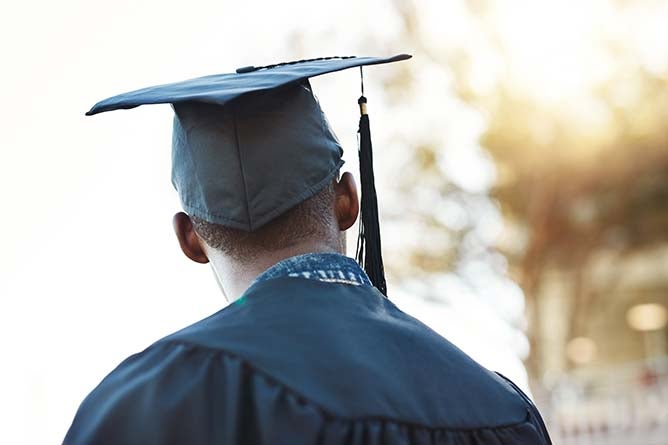 A new graduate looks off into the distance wearing cap and gown.