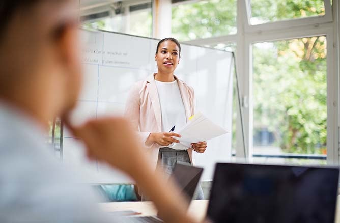 leadership theories tasks An educational leader heads a group meeting while standing in front of whiteboard.
