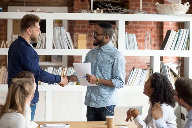 Two employees shake hands because of a job well done.
