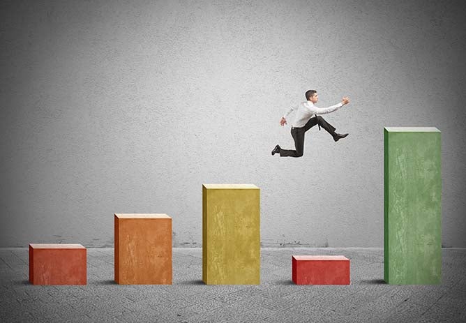 A man leaps above a low block in a bar graph.