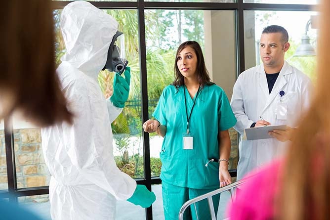A nurse and doctor speak to a person in biohazard gear.