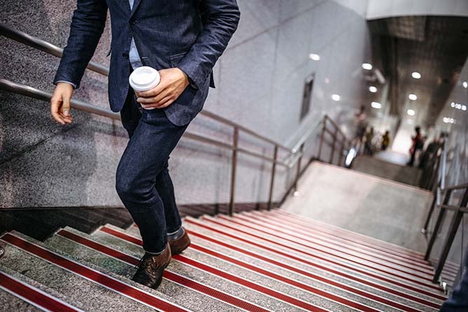 A businessman climbs the stairs with coffee in hand.