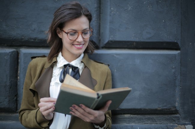 Woman against wall reading book for PhD