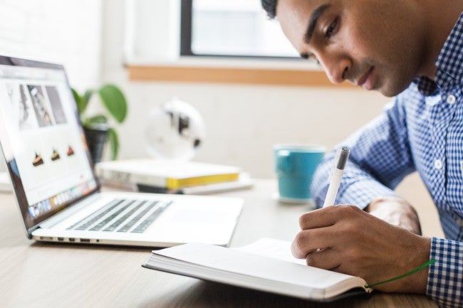 Health information technician taking notes while looking at computer