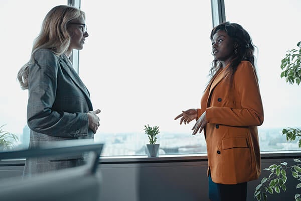 Two women standing in front of a window, negotiating