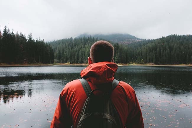 A man in a red jacket looks out over a lake.