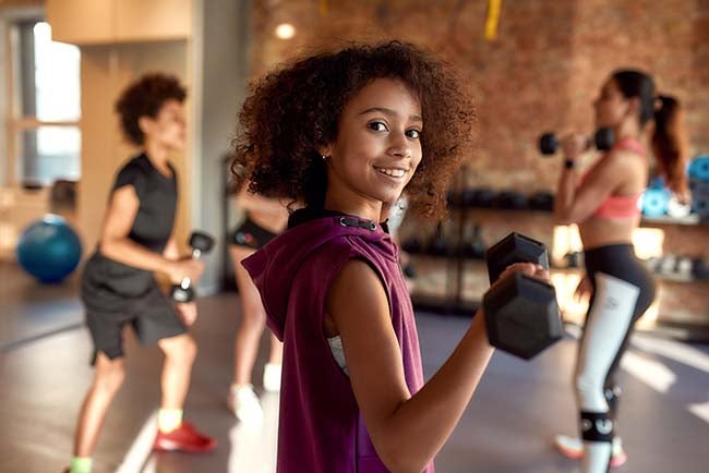 A young girl does bicep curls in a fitness course.