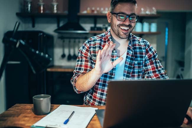 A young man uses a laptop in his kitchen while getting some work done.