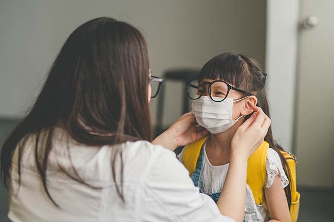 A mother helps her young daughter don a facemask.