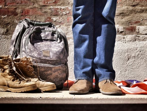 Person in casual clothes standing next to military fatigues and backpack