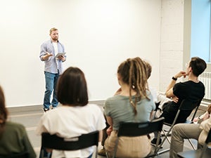 Man instructing adults seated on folding chairs
