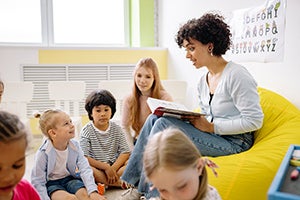 Teacher seated on a beanbag reading to young students