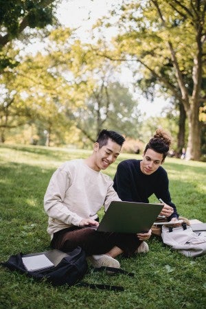two happy students outside with a laptop