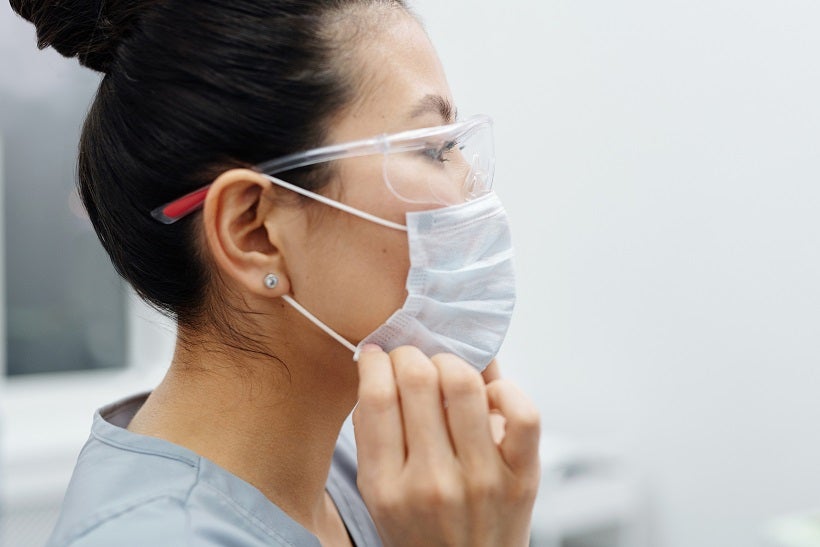 person in scrubs and protective glass positioning a mask