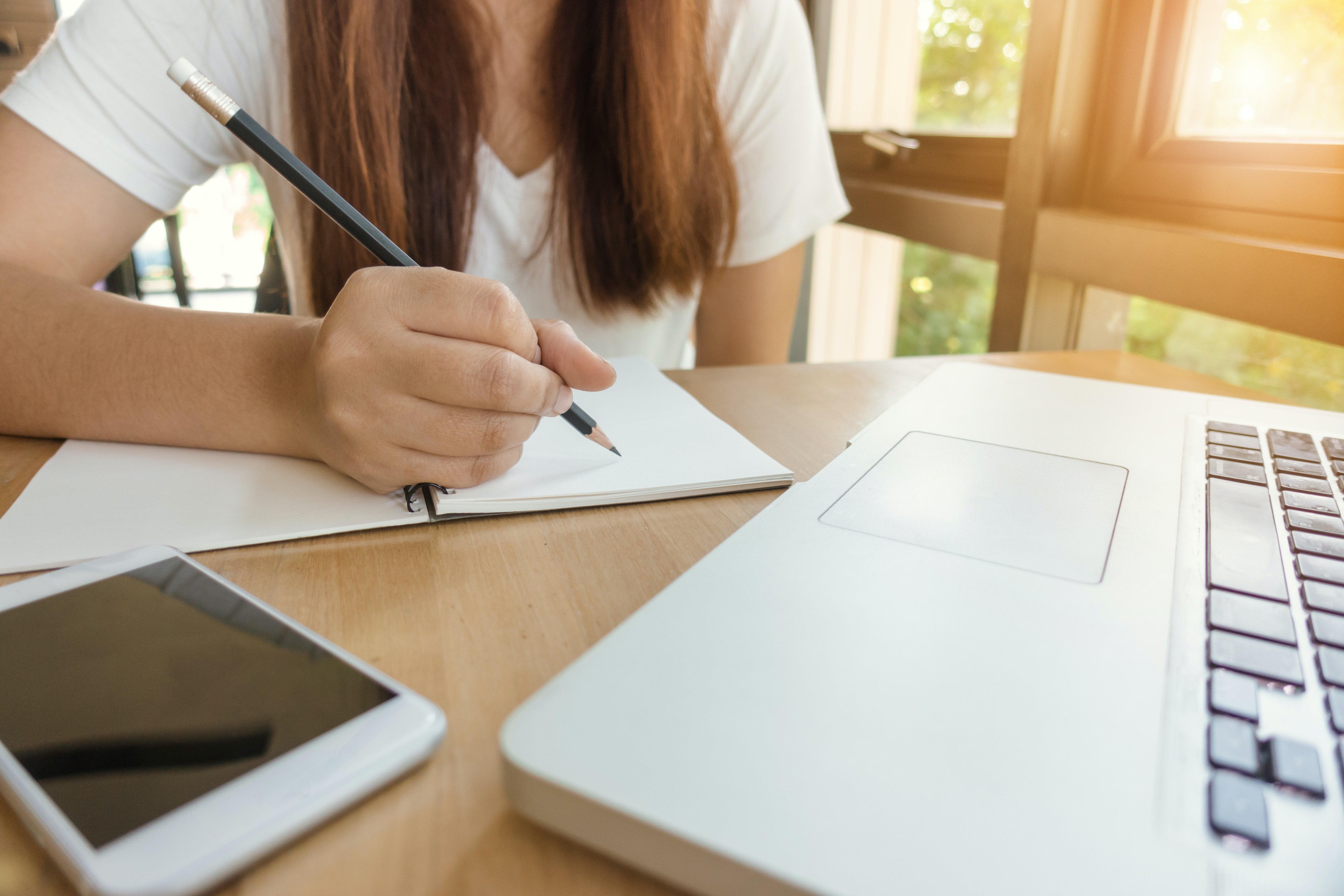 a person writing in a notebook with a laptop computer open in front of them
