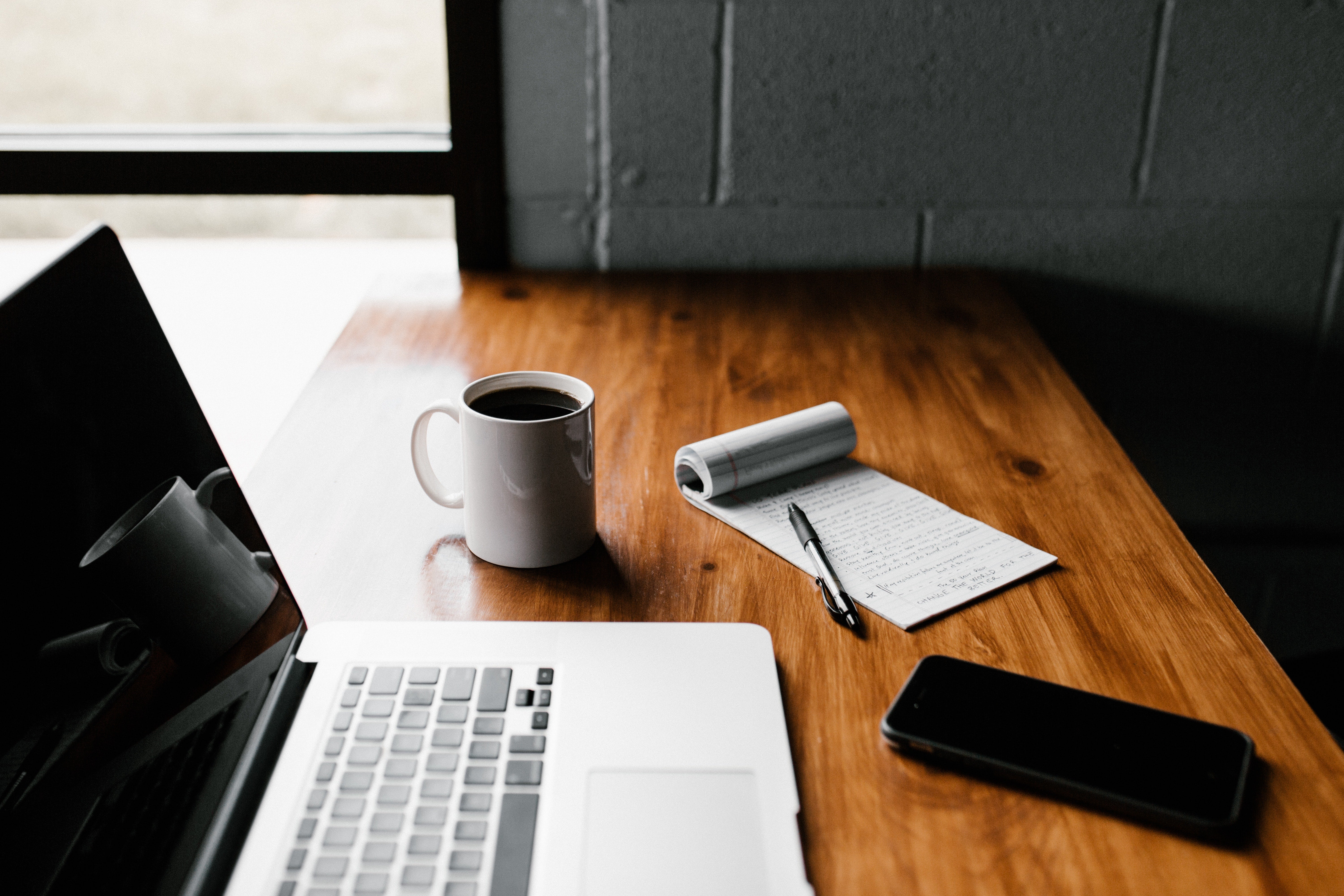 Laptop, cup of coffee, notebook and phone sitting on a wooden desk
