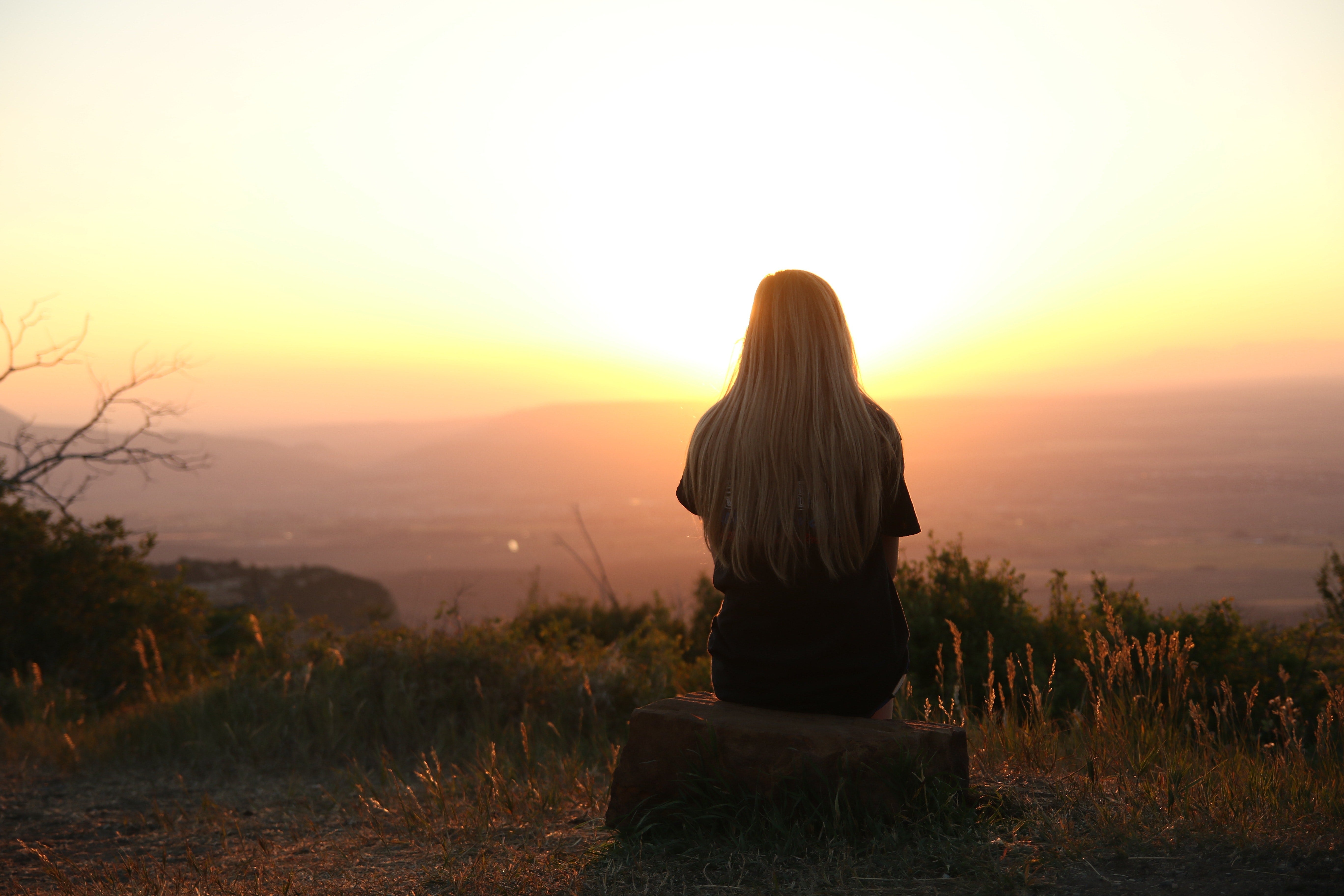 Person facing away from the camera on a mountain looking at a sunset.