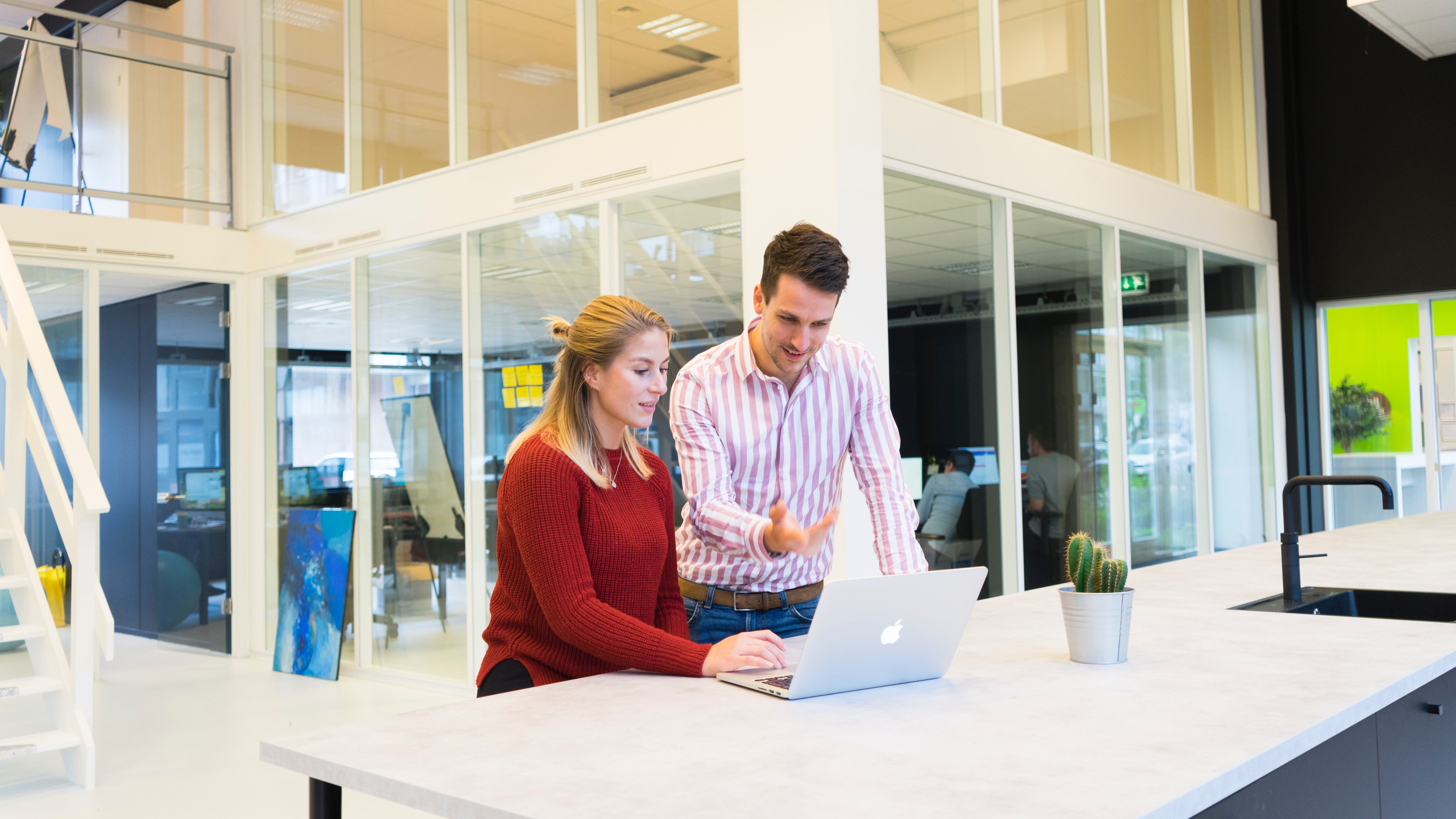 two people standing at a table looking at a laptop