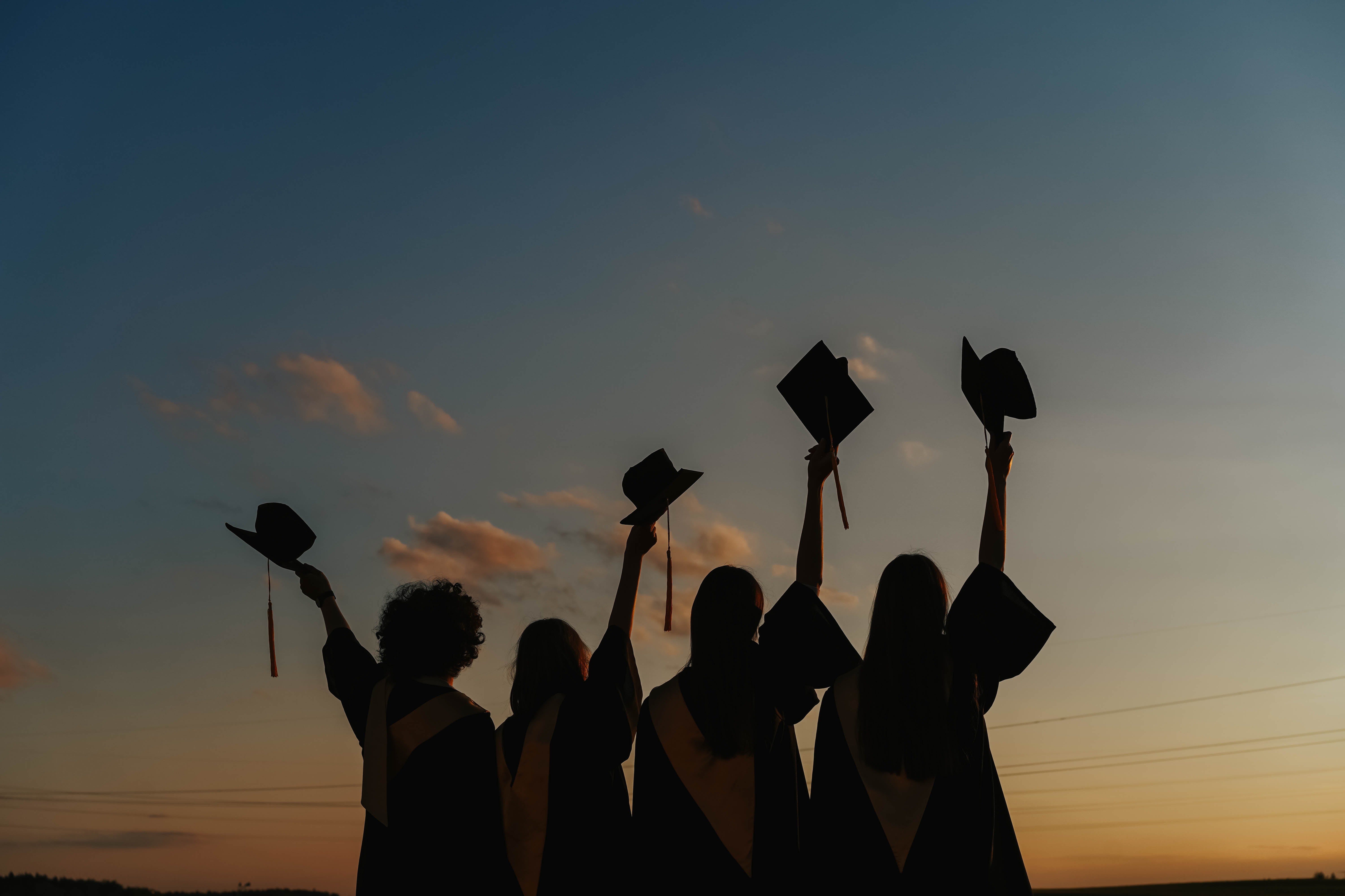 silhouette of people holding graduation caps in the air