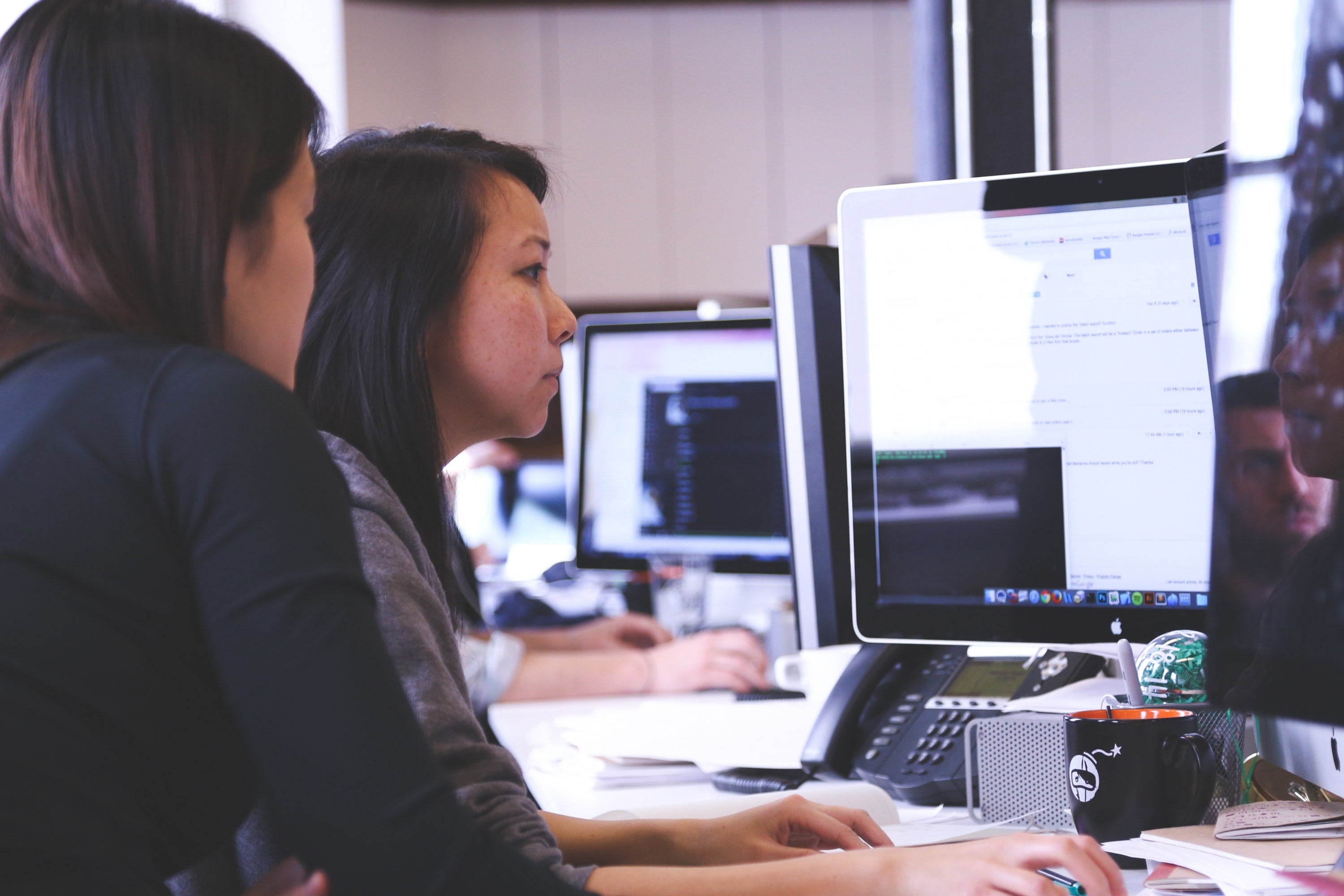 two people at a desk looking at a screen