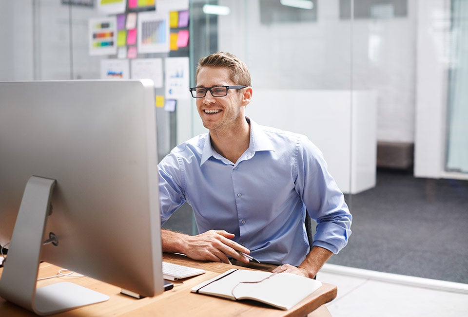 White IT Professional Man Sitting and Smiling at Desktop Computer