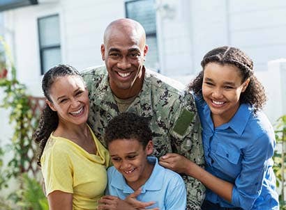 Man in armed forces uniform with spouse and two kids smiling at the camera