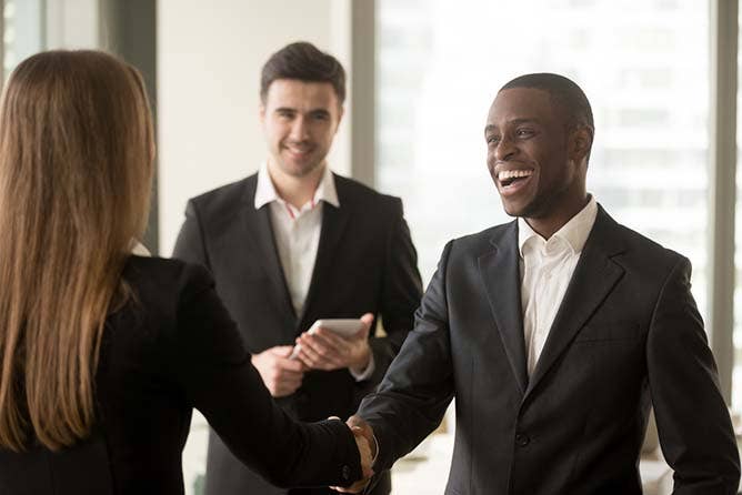 Happy smiling businessman and businesswoman shaking hands standing in modern office