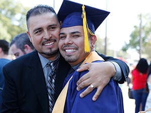 Graduate, in cap and gown, being hugged by his father.