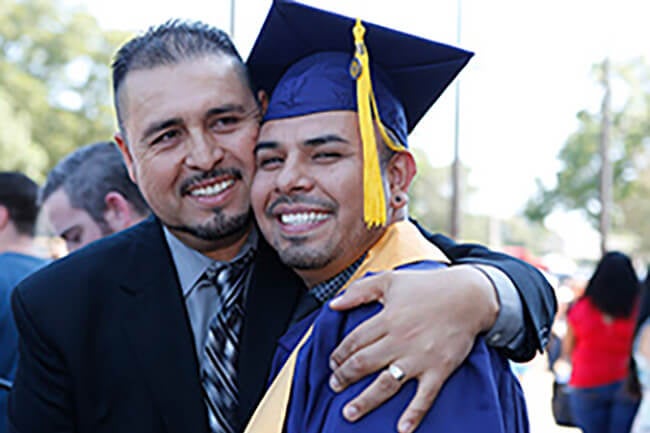 Graduate, in cap and gown, being hugged by his father.