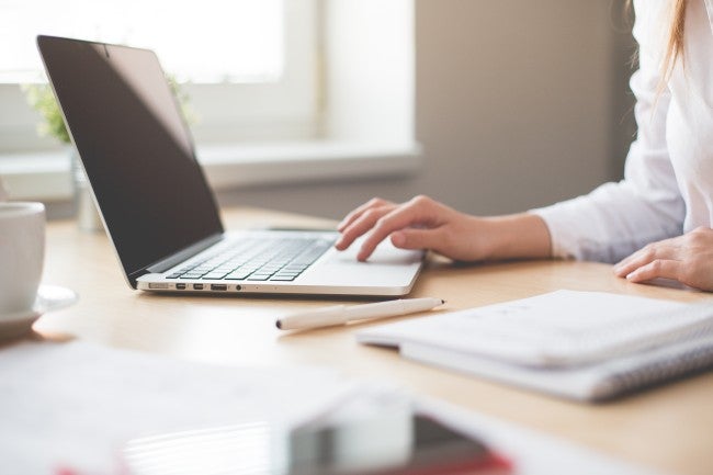 Hand on computer next to notepad - business analyst