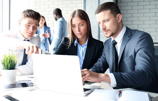 3 people working around a laptop together 