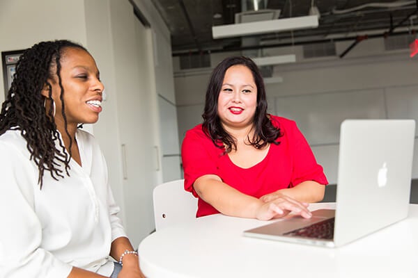 two women talking and smiling while working around a ccoputer