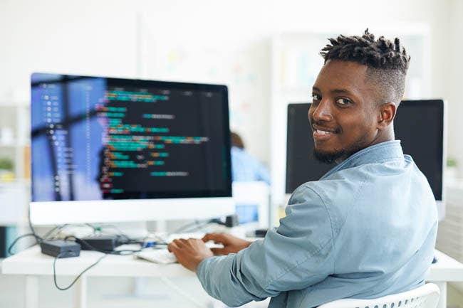 Software developer looking at you while sitting by workplace computer