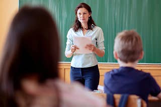 Female teacher reading off paper in front of classroom