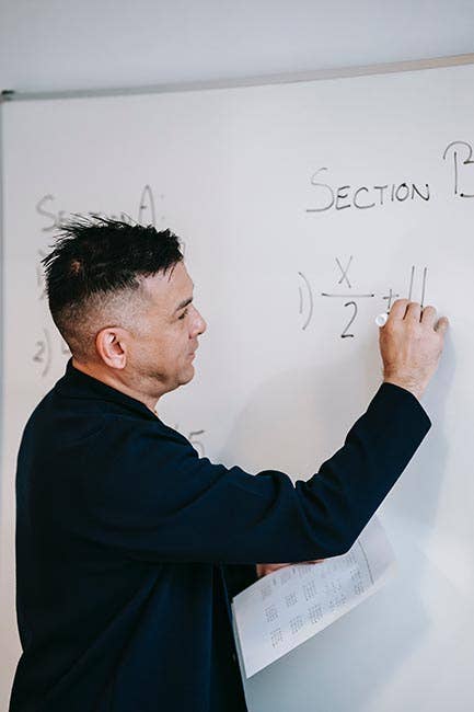 Math teacher solving problem on a whiteboard in class