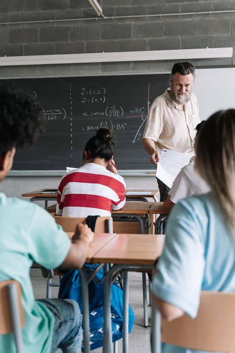 High school math teacher hands out papers to a class of students