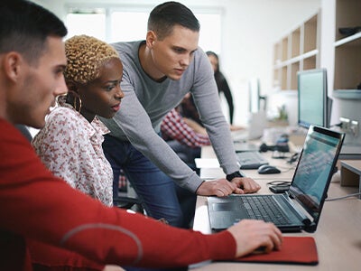 Three professionals looking at one laptop together
