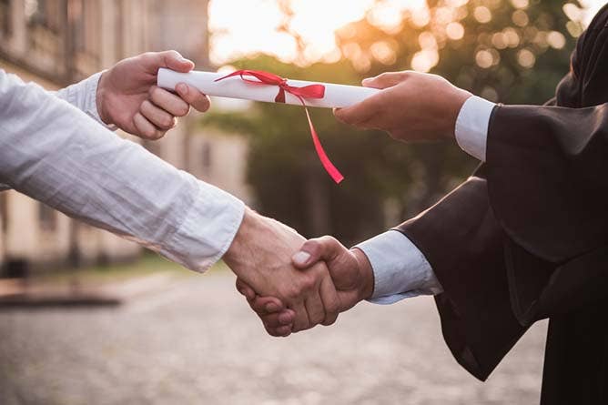 Employer and college graduate shaking hands holding a diploma