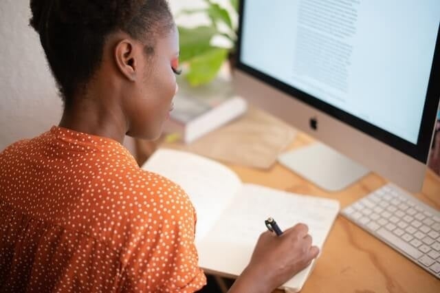 young woman writing on a notebook in front of her computer