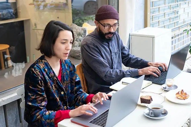 Man and woman each with a laptop sitting side by side