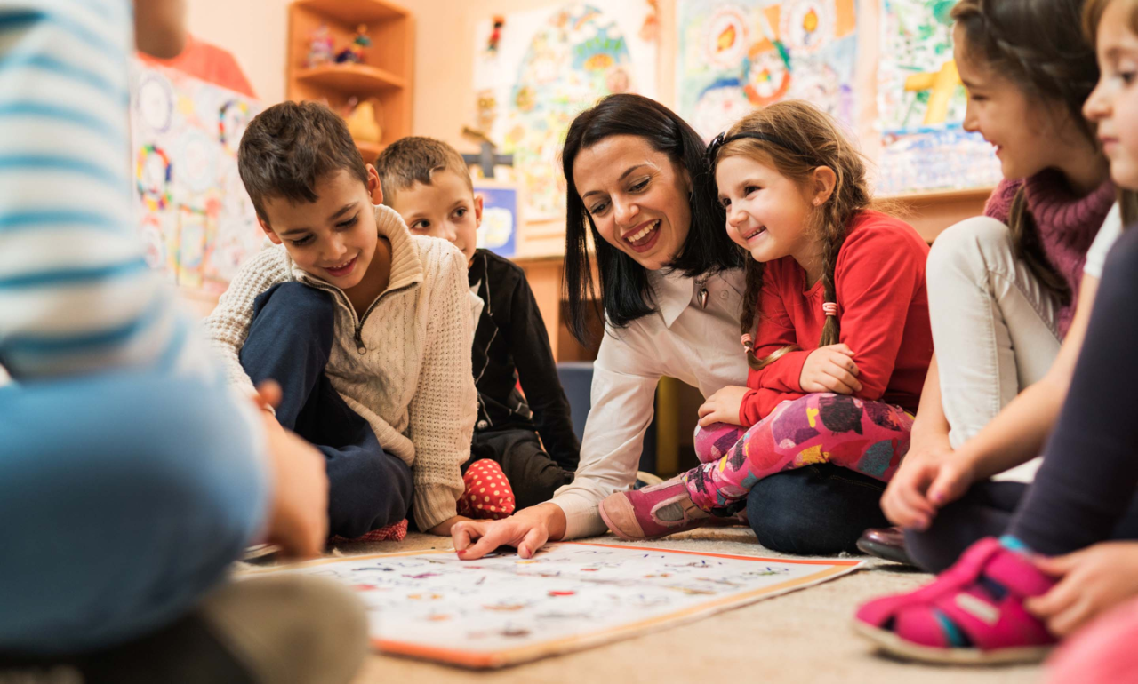 Happy female teacher teaching group of small kids in a preschool.