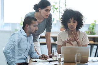 group of adults studying together around a laptop