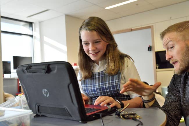 In a classroom, a teacher guides a preteen student through a lesson on a laptop.