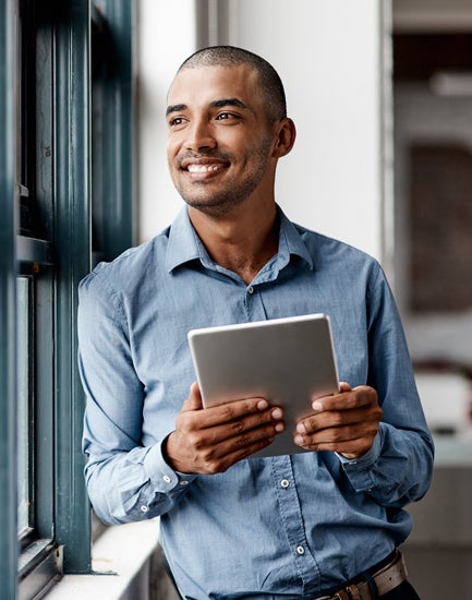 Man looking outside of a window while holding a tablet