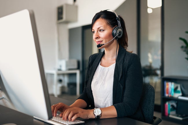 Woman with headset on typing at large desktop computer