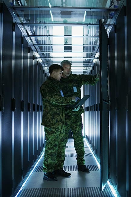 In Data Center Two Military Men Work with Open Server Rack Cabinet. One Holds Military Edition Laptop.