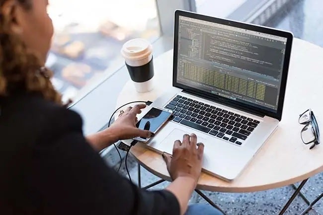 Woman working remotely with a phone connected to the laptop