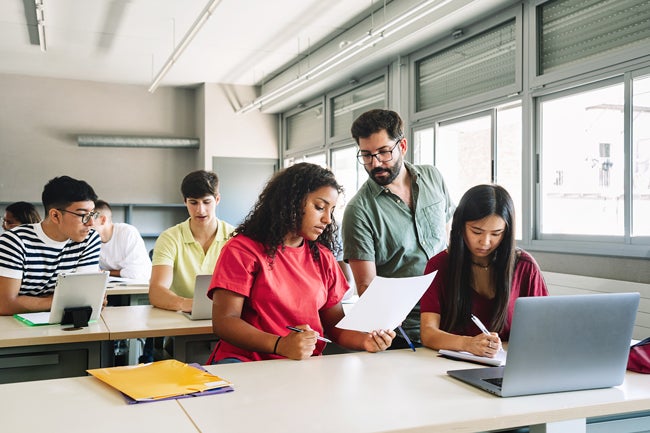 Male teacher helping high school students on their reports