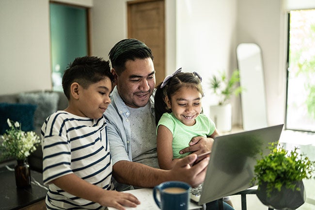 Father with his kids using laptop and mobile phone watching something at home