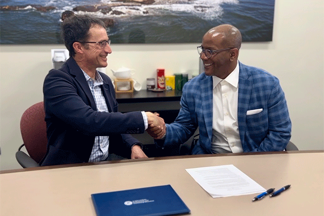 Two men at table shaking hands and signing documents for UC Santa Barbara Extension